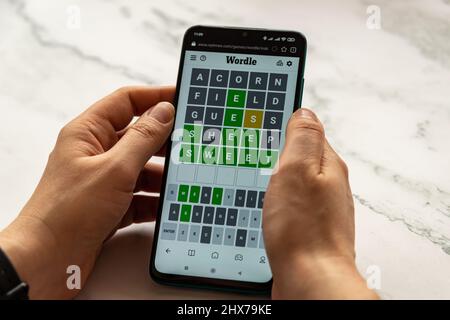 Hände spielen Wordle Spiel auf dem Telefon auf NYTimes.com Website. Wordle ist ein webbasiertes Wortspiel, das von Josh Wardle erstellt und entwickelt wurde. Es ist ein sehr beliebtes W Stockfoto