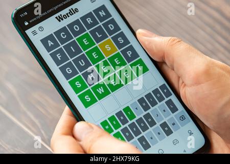 Hände spielen Wordle Spiel auf dem Telefon auf NYTimes.com Website. Wordle ist ein webbasiertes Wortspiel, das von Josh Wardle erstellt und entwickelt wurde. Es ist ein sehr beliebtes W Stockfoto