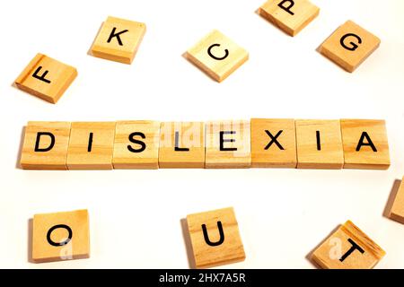 Hölzerne Alphabetische Blöcke mit LEGASTHENIE-Wort in der Mitte auf weißem Hintergrund. Konzept der Dyslexie-Bewusstsein und menschliche Gehirnentwicklung Stockfoto