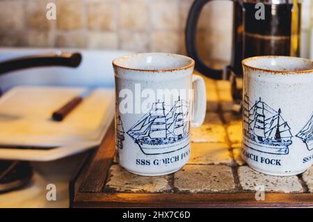 Zwei Porzellan-Kaffeetassen auf der Küchentheke mit der Wand und der Kaffeedose im Hintergrund verschwommen Stockfoto