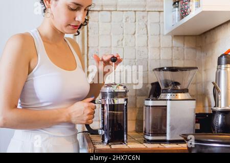 Die junge kaukasische Frau in ihrer Küche bereitet Kaffee mit einer manuellen kaffeemaschine für französische Pressen auf der Theke, im Café und im Lifestyle-Konzept zu. Stockfoto