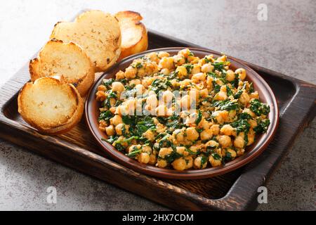 Spinat mit Kichererbsen mit Gewürzen, Knoblauch und Essig in einer Schüssel auf einem Holzbrett. Horizontal Stockfoto
