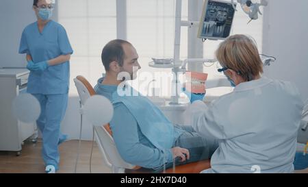 Zahnarzt, der dem Patienten Hygienestunde gibt, um die Zähne mit Zahnbürste und Zahnpasta in der Stomatologie richtig zu reinigen. Experte zeigt Mundpflege Routine auf künstlichen Kiefer, um Karies zu verhindern. Stockfoto