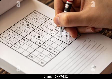 Person, die ein Sudoku-Puzzle auf einem Holztisch löst. Stockfoto