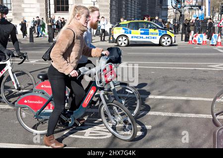 Ein Paar, das den Fahrradverleih in London benutzte. Hier in Westminster, im Zentrum von London. Das Leihfahrrad, das mehr umweltfreundlichen Verkehr fördert, wurde 2010 eingeführt; die Barclays Bank war der erste Sponsor und Santander ab 2015. Obwohl es nach dem damaligen Bürgermeister von London allgemein als „Boris Bikes“ bekannt war, wurde das Konzept zunächst vom früheren Bürgermeister, Ken Livingtone, promotet. Stockfoto