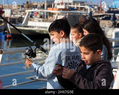 ASCHKELON, ISRAEL - 04. MÄRZ 2022: Kinder gehen im Hafen von Aschkelon fischen. Konzentrieren Sie sich auf den Jungen mit der Angelrute. Unscharfer Hintergrund. Stockfoto