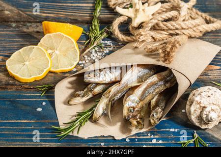 Sonnengetrockneter Geruch in einer Papierverpackung. Gesalzener Fisch im marinen Stil. Zitrone, frischer Rosmarin, Seeseil. Blauer nautischer Holzhintergrund, Nahaufnahme Stockfoto