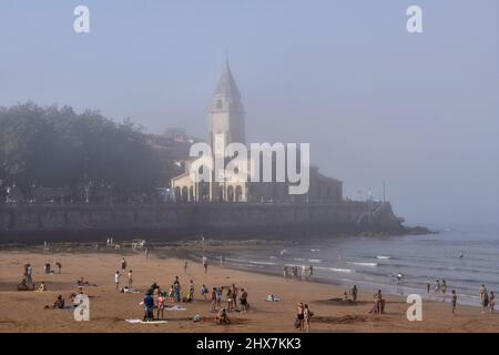 Menschen Urlauber am Strand Playa de San Lorenzo mit Kirche San Pedro im Hintergrund. Nebliger Sommernachmittag in Gijon Asturias Spanien. Stockfoto