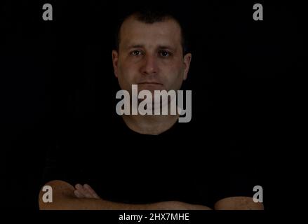 Der Mann faltete seine Arme auf einem schwarzen Hintergrund Stockfoto