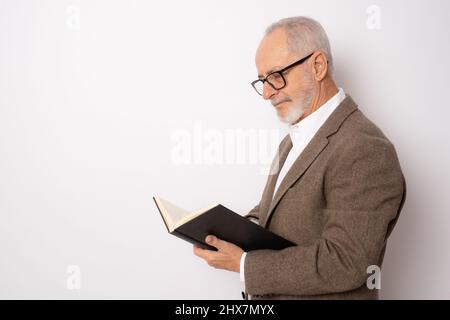 Porträt eines älteren Mannes in eleganter Kleidung, der ein Buch liest, das isoliert auf weißem Hintergrund steht. Stockfoto