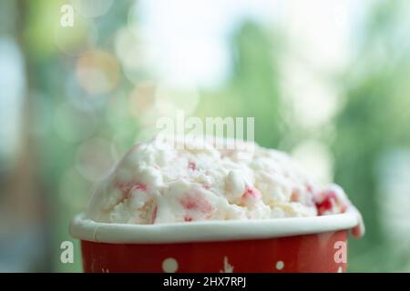 Bunte Eisschaufeln in roter Schale, auf weichem grünem Kopierraum Hintergrund, Eisschaufeln in Tasse mit Schokolade, Vanille und Erdbeere Stockfoto
