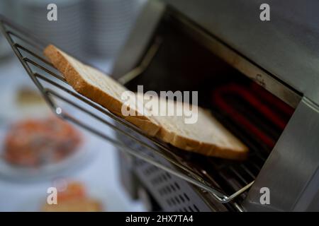 Heiß geschnittenes geröstetes Brot zum Frühstück im Toaster auf dem Küchentisch des Elektroofens Stockfoto