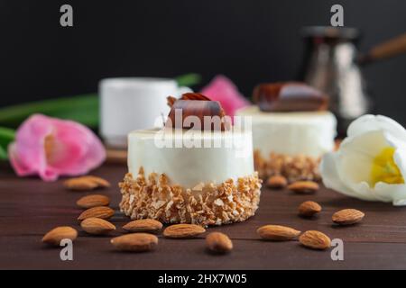 Zwei Cupcakes mit schokoladenweißer Kaffeetasse, Mandel und Tulpen auf einem Holztisch. Selektiver Fokus Stockfoto