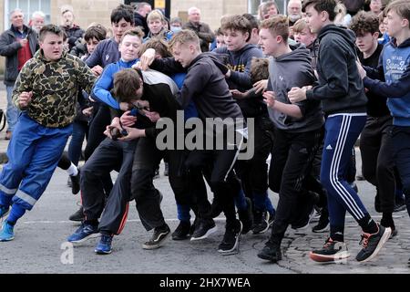 Jedburgh, Donnerstag, 10. März 2022. Ein nicht identifizierter Jugendlicher mit 'Ba' in der Hand wird von anderen herausgefordert, dass die 'Schule Ba' die erste ist, die zu Beginn der jährlichen 'Fastern Eve Handba'-Veranstaltung in der High Street in den Scottish Borders von Jedburgh am 10. März 2022 in Jedburgh, Schottland, 'gefeiert' wird. Die jährliche Veranstaltung, die im 18. Jahrhundert begann, findet heute statt und umfasst zwei Teams, die Uppies (Bewohner aus dem oberen Teil von Jedburgh) und die Doonies (Bewohner aus dem unteren Teil von Jedburgh), die den Ball entweder auf den oberen oder unteren Rand der Stadt bringen. Der Ball, der aus Leder besteht, ist mit gestopft Stockfoto