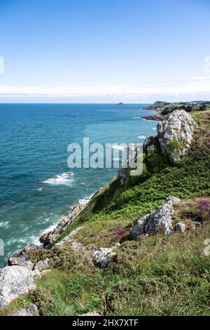 Grün bewachte Klippen fallen steil in den stark blau leuchtenden Atlantik im Norden der Bretagne.kleine Segelboote schweben in der Sonne auf dem Meer. Stockfoto