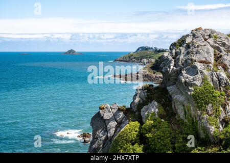 Grün bewachte Klippen fallen steil in den stark blau leuchtenden Atlantik im Norden der Bretagne.kleine Segelboote schweben in der Sonne auf dem Meer. Stockfoto