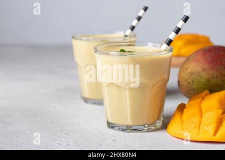Mango Lassi in zwei Gläsern auf hellgrauem Hintergrund mit Kopierraum. Frische indischer Lassi aus Joghurt, Wasser, Gewürzen, Mango und Eis Stockfoto