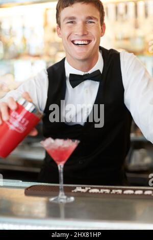 Löscht den Durst der Ladys. Der junge, gutaussehende Barkeeper lachte und lächelte, während er einen köstlichen und leckeren Cocktail abwischte. Stockfoto