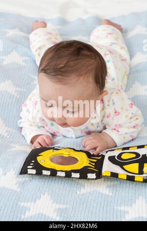 Baby liegt auf der Vorderseite auf weicher Oberfläche und schaut in den Spiegel im Materialbuch Stockfoto