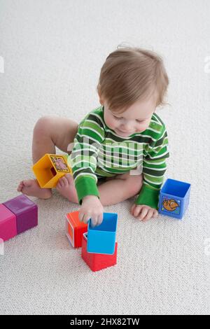 Der kleine Junge saß auf dem Teppich und spielte mit bunten Blöcken Stockfoto