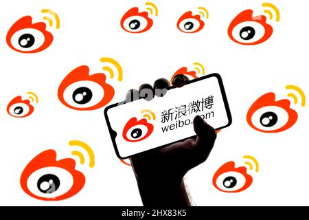 Smartphone mit chinesischem Weibo Microblogging-Service-Logo auf dem Bildschirm in geballter Hand auf dem Hintergrund der Weibo-Logos Stockfoto