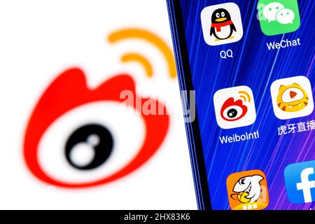 Das Symbol der chinesischen Microblogging-Service-Anwendung Weibo unter anderem auf dem Smartphone-Bildschirm. Auf dem Hintergrund ist das Weibo-Logo zu sehen. Stockfoto
