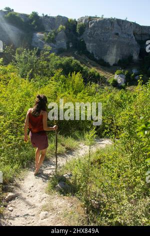 Mädchen geht entlang Bergweg. Gehen Sie in freier Wildbahn. Tourist steigt aus den Bergen. Ruhe im Sommer. Frau mit Stock in den Händen geht unbekannte Straße unter Stockfoto