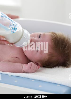 Baby Junge liegt auf Wechselmatte und wird Milch aus einer Flasche gefüttert, 8 Wochen Stockfoto