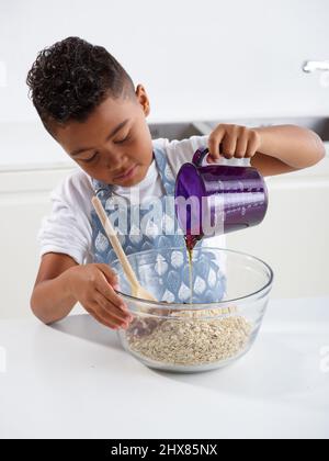 Fruchtiges Beerengranola -ÔøΩPouring Honig in eine Schüssel voller Hafer und Nüsse (Schritt 2 von 4) Stockfoto