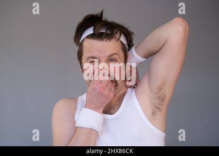 Sportler mit Retro-Schnurrbart schnüffelt angewidert seine verschwitzte Achselhöhle Stockfoto