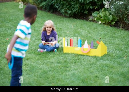 Kinder spielen im Garten mit Pappring werfen Spiel Stockfoto