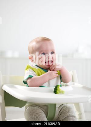 Baby im Alter von 6 Monaten essen im Hochstuhl Stockfoto