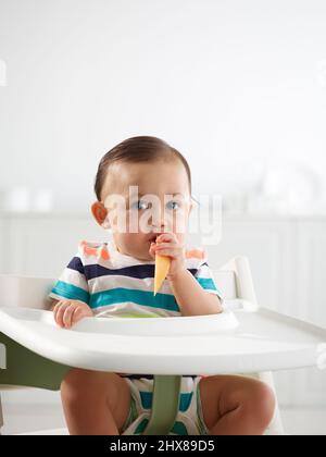 Baby im Alter von 10 Monaten essen im Hochstuhl Stockfoto