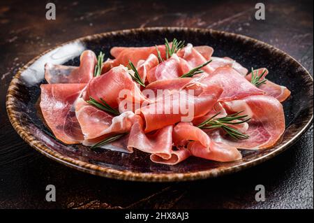 Scheiben Prosciutto crudo parma oder Jamon serrano mit Rosmarin. Dunkler Hintergrund. Draufsicht Stockfoto