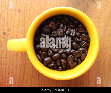 Geröstete ganze Kaffeebohnen in einem leuchtend gelben Becher Stockfoto