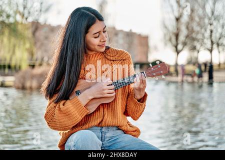 Portrait der Latina Frau spielt Ukulele. Brunette hispanische Frau mit langen Haaren Stockfoto