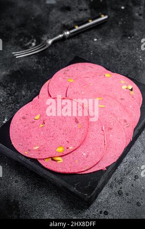 Fleischsalami-Wurstscheiben mit Pistazien-Nüssen auf Marmorplatte. Schwarzer Hintergrund. Draufsicht Stockfoto