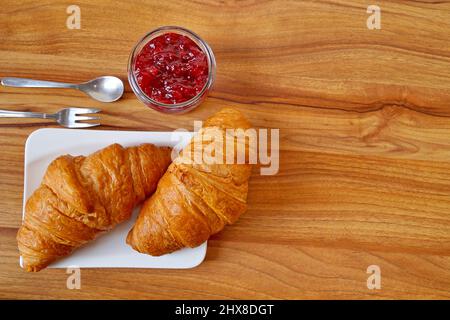 Zwei Croissants liegen auf einem weißen Teller neben einem Glas mit Beerenmarmelade. Das Foto ist quadratisch. Stockfoto