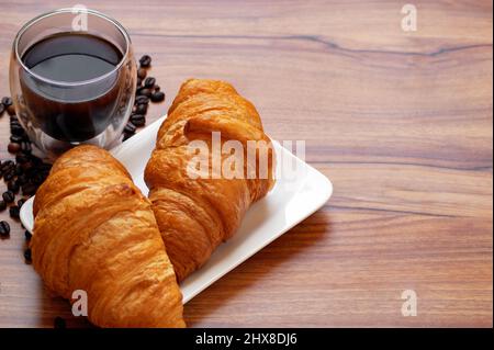 Kaffee, frisch gebackene Croissants mit knuspriger Kruste auf einem Holztisch Kaffee, frisch gebackene Croissants mit knuspriger Kruste auf einem Holztisch Stockfoto
