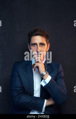 Hübscher Geschäftsmann, der mit gekreuzten Armen vor grauem Hintergrund steht. Stockfoto