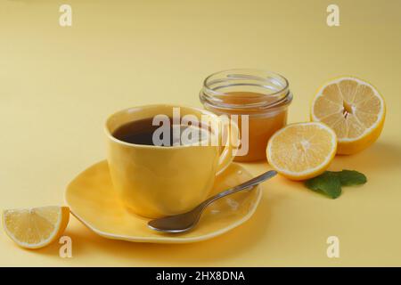 Gelbe Zitronen, Tee in einer gelben Tasse, ein Glas Honig sind diagonal angeordnet. Tabellenhintergrund - gelb Stockfoto