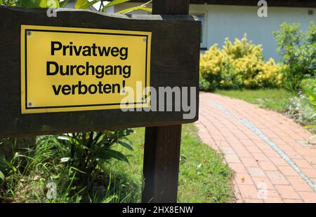 Gelbes Warnschild mit dem deutschen Text 'Privatweg Durchgang verboten', der in englischer Sprache in 'Private Way Passage forbidden' übersetzt wird Stockfoto