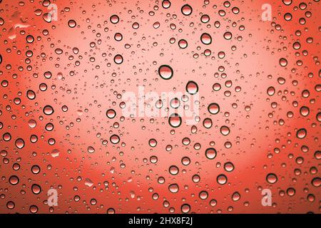 Regentropfen auf einem Glasfenster, roter Hintergrund Stockfoto