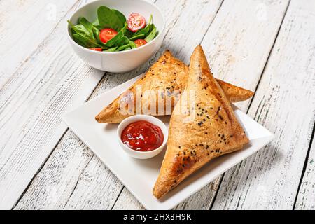 Teller mit leckeren usbekischen samsa und Tomatensauce auf weißem Holzhintergrund Stockfoto