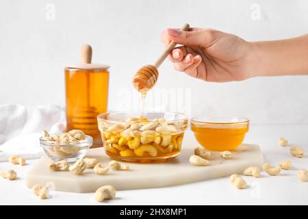 Weibliche Hand mit Dipper und süßen Cashewnüssen in Honig auf hellem Hintergrund Stockfoto