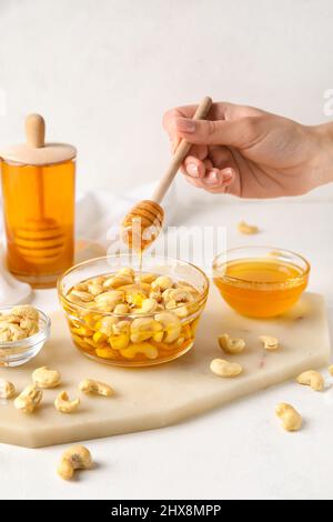 Weibliche Hand mit Dipper und süßen Cashewnüssen in Honig auf hellem Hintergrund Stockfoto