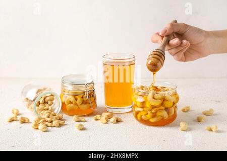 Weibliche Hand mit Dipper und süßen Cashewnüssen in Honig auf hellem Hintergrund Stockfoto