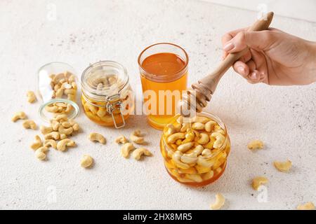 Weibliche Hand mit Dipper und süßen Cashewnüssen in Honig auf hellem Hintergrund Stockfoto