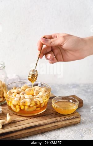 Weibliche Hand mit Dipper und süßen Cashewnüssen in Honig auf hellem Hintergrund Stockfoto