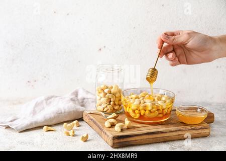 Weibliche Hand mit Dipper und süßen Cashewnüssen in Honig auf hellem Hintergrund Stockfoto